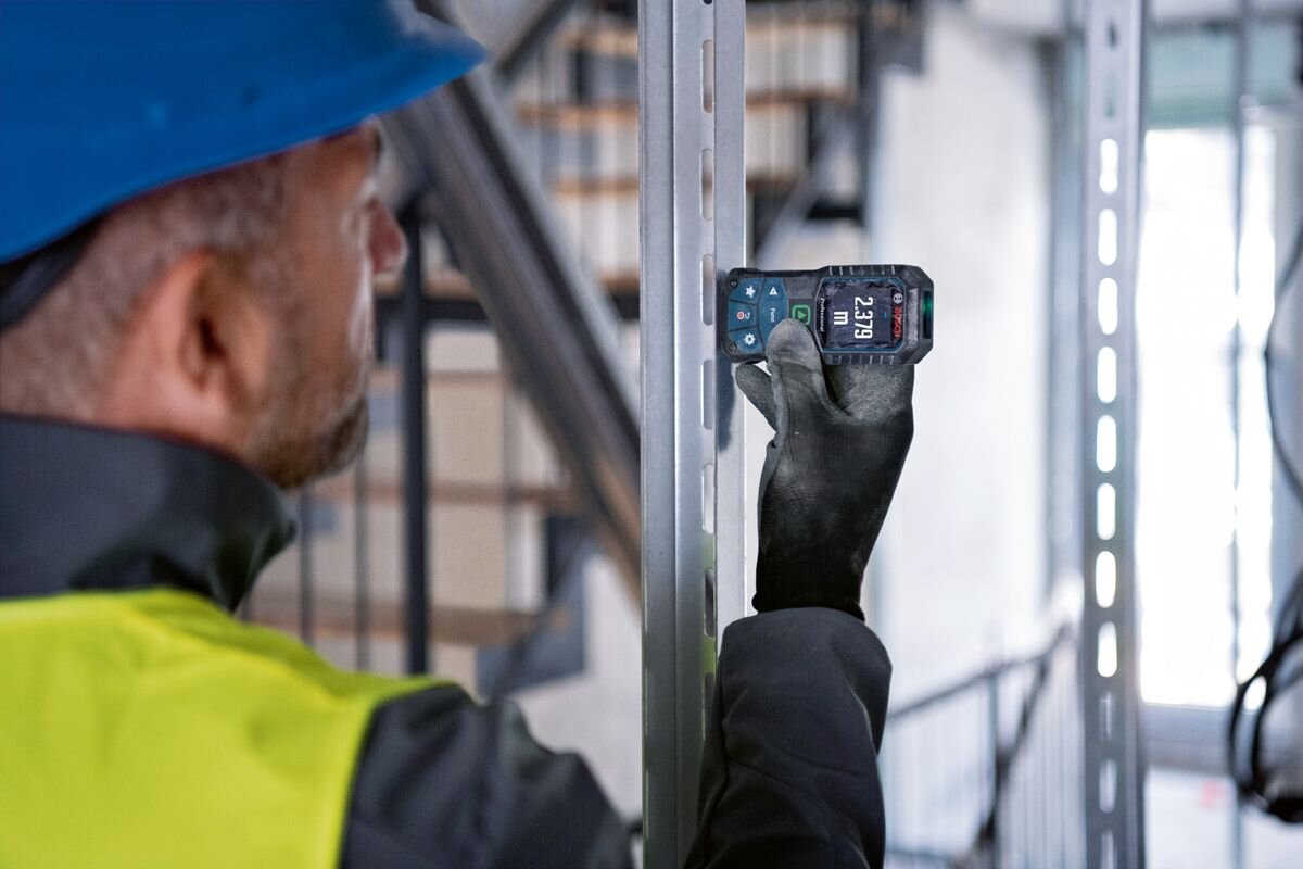 Dalmierz laserowy BOSCH GLM 50-25 G 50m, pomiar, laser, odległość, praca, mężczyzna trzyma dalmierz przy ścianie i odmierza dystans