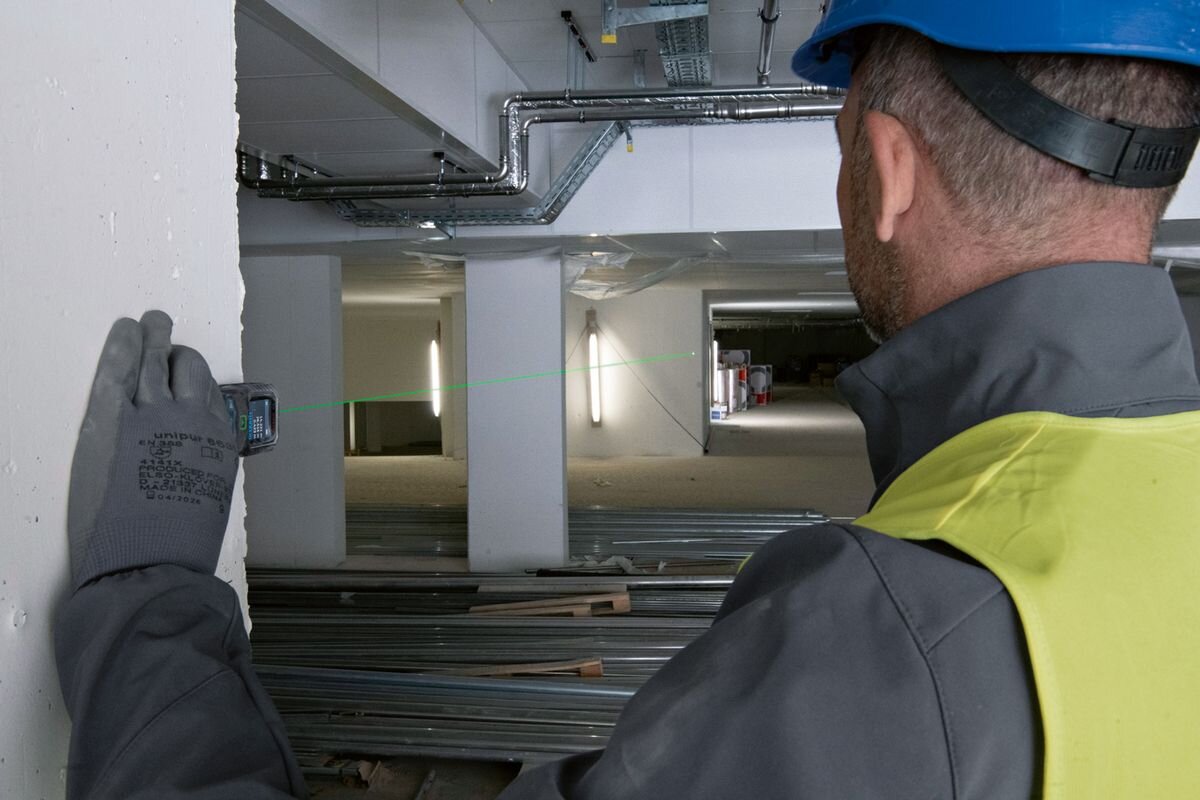 Dalmierz laserowy BOSCH GLM 50-25 G 50m, laser, zielony, precyzja, widoczność, mężczyzna trzyma dalmierz przy ścianie i odmierza dystans