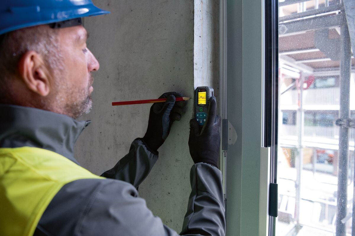 Dalmierz laserowy BOSCH GLM 50-25 G 50m, menu, ekran, obliczenia, funkcje, mężczyzna oznacza na ścianie wymiary dzięki dalmierzowi