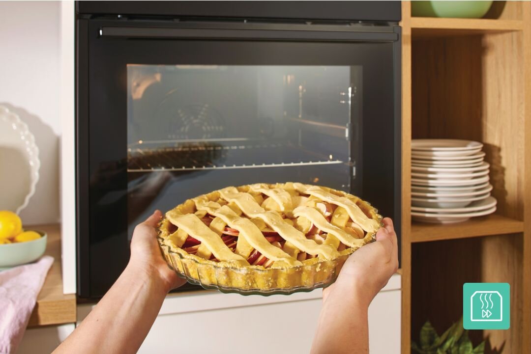 PIEKARNIK GORENJE BO6735E05B Tarta z kratką z ciasta jest trzymana oburącz przed otwartym piekarnikiem do zabudowy. Ujęcie pokazuje wygodne wkładanie potraw do nagrzanego urządzenia