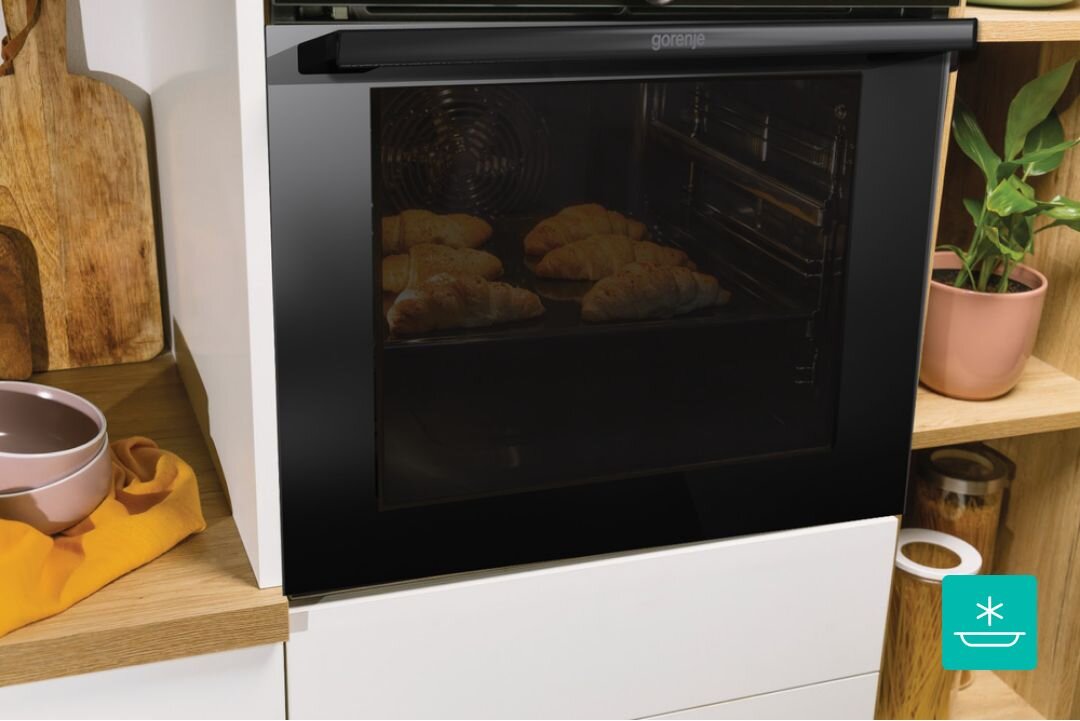 PIEKARNIK GORENJE BO6735E05B Piekarnik Gorenje w zabudowie z widocznymi rogalikami piekącymi się w środku. Przez przyciemnione szkło widać równomiernie zarumienione wypieki