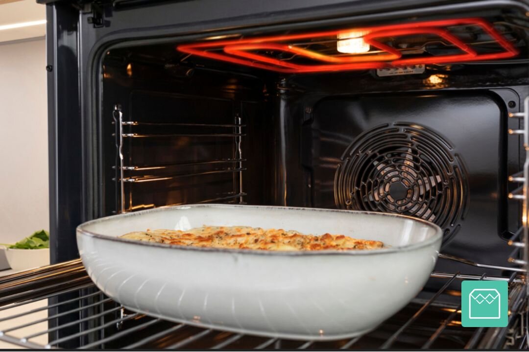 PIEKARNIK GORENJE BO6735E05B Naczynie żaroodporne z zapiekanką znajduje się wewnątrz piekarnika z włączoną górną grzałką. Ujęcie podkreśla równomierne zapiekanie potrawy i nowoczesne wnętrze komory