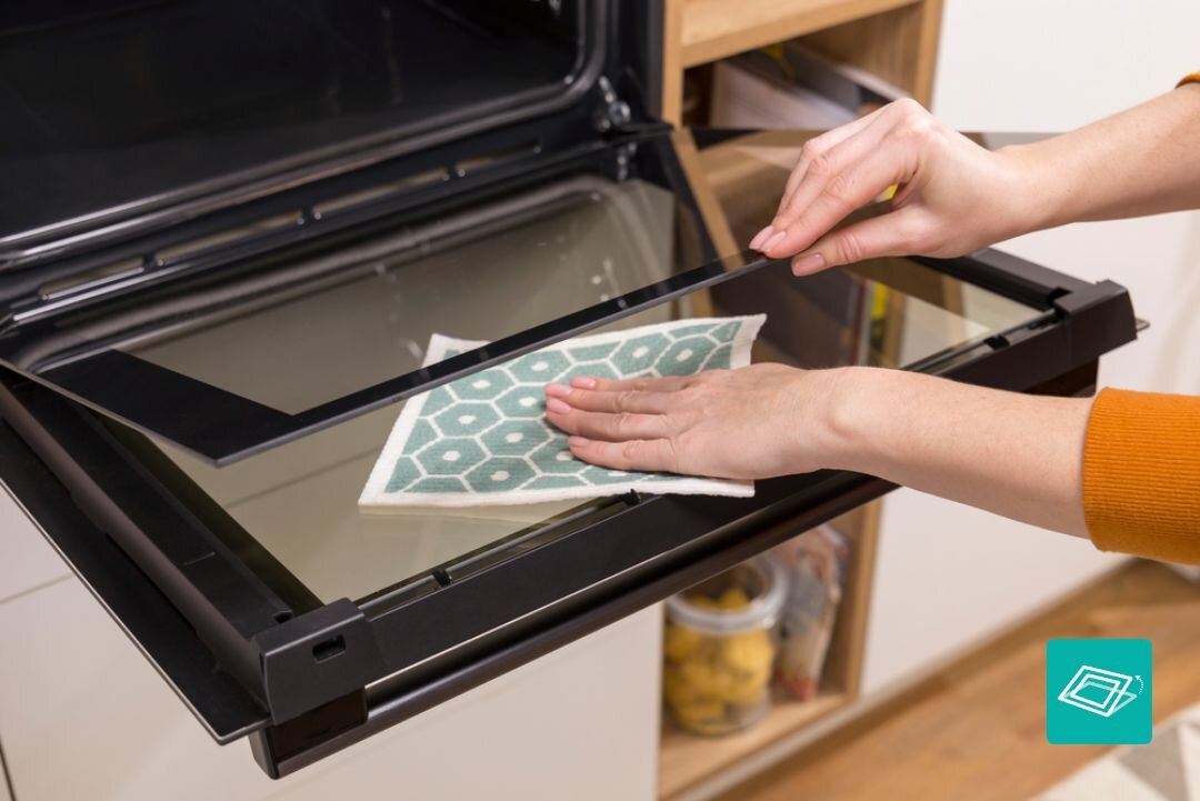 PIEKARNIK GORENJE BSA6737E15BG Czyszczenie wewnętrznej strony drzwi piekarnika przy użyciu ściereczki, przy całkowicie otwartym froncie. Ujęcie podkreśla łatwy dostęp i prostą pielęgnację gładkiej szklanej powierzchni