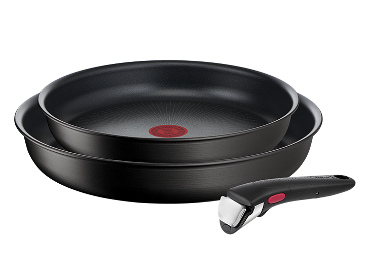 Na obrazie widoczne są dwie czarne patelnie z czerwonym okrągłym wzorem na środku oraz odłączana rączka. Patelnie mają gładką powierzchnię i są ułożone jedna na drugiej.