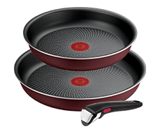 Na obrazie widoczne są dwie patelnie o ciemnym wnętrzu z czerwonym wzorem na środku oraz odłączana rączka. Patelnie mają zewnętrzną powierzchnię w kolorze bordowym.