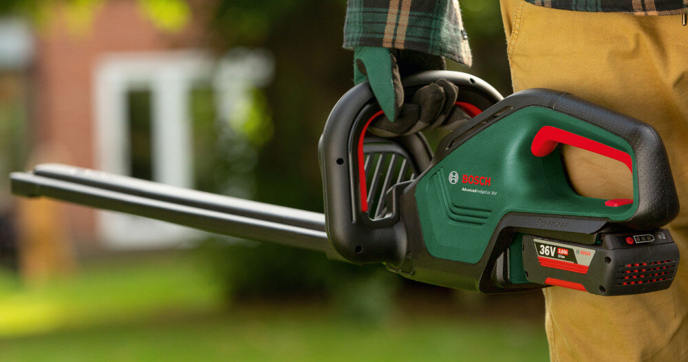 Nożyce do żywopłotu BOSCH AdvancedHedgeCut 36V-65-28 060084A301 akumulatorowe ogród osoba trzyma nożyce w dłoni w tle dom współpracuje z akumulatorami z serii POWER FOR ALL 36 V pełna swoboda ruchu i mobilność akumulator kompatybilny z innymi narzędziami z tej serii oszczędność czasu i pieniędzy