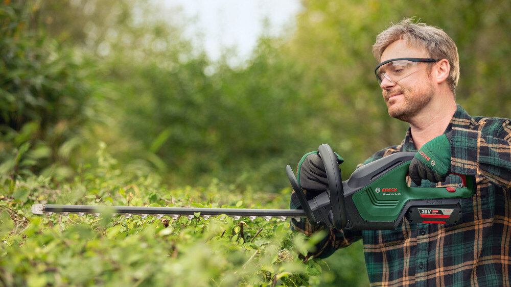 Nożyce do żywopłotu BOSCH AdvancedHedgeCut 36V-65-28 060084A301 akumulatorowe ogród osoba tnie żywopłoty trzymając nożyce w dłoniach opatentowany system BOSCH Anti Blocking zapobiega blokowaniu się noży podczas cięcia gęstych gałęzi cięcie odbywa się płynnie i bez przerw bezpieczeństwo pracy