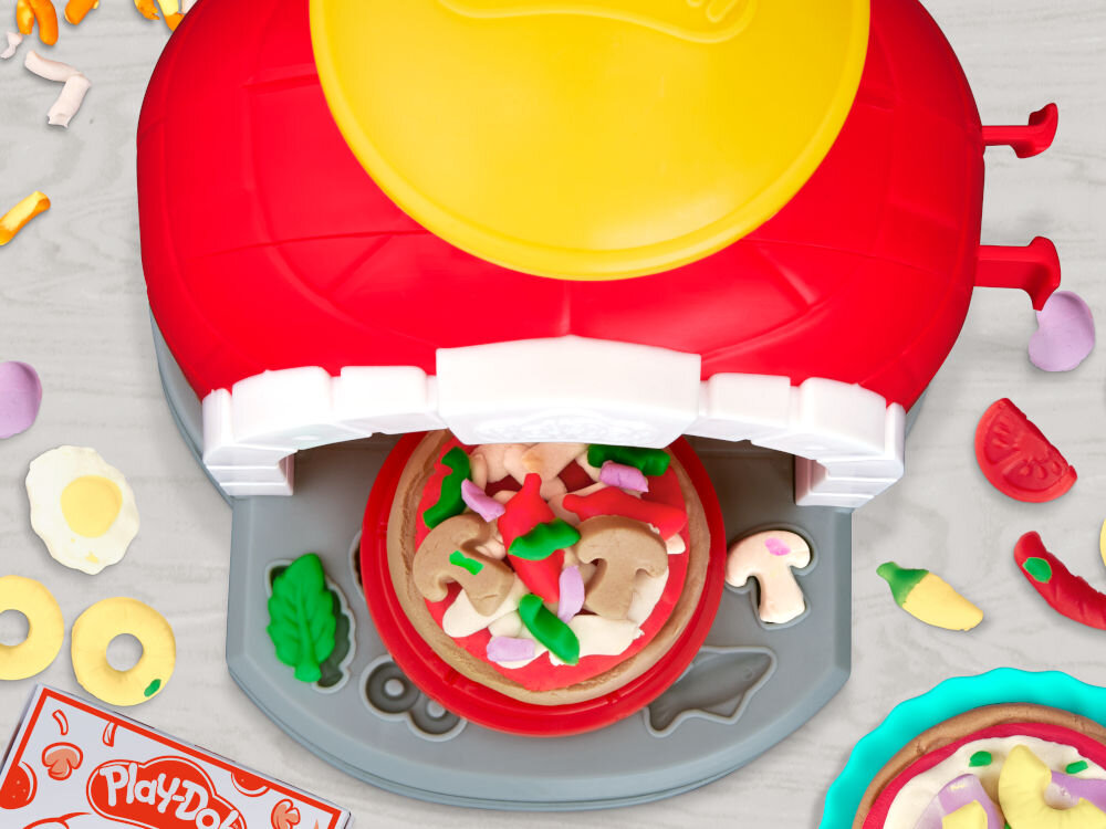 Zestaw do zabawy z ciastoliną przedstawia piec do pizzy z czerwonym i żółtym elementem oraz różnorodne kształty przypominające składniki pizzy. Widoczne jest logo \'Play-Doh\' na opakowaniu.