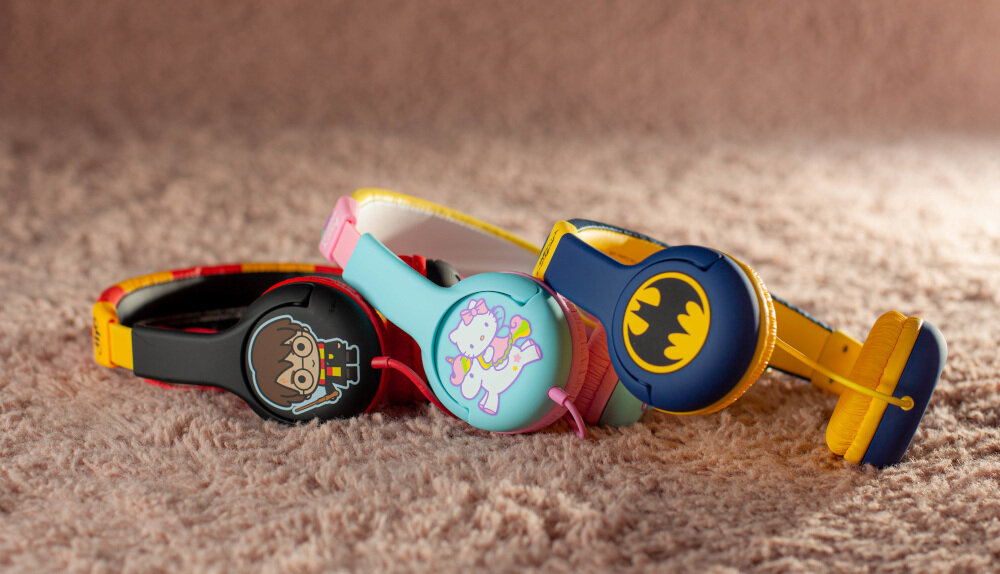 Na obrazie widoczne są trzy pary kolorowych słuchawek nausznych z motywami postaci i symboli. Słuchawki leżą na miękkim, beżowym podłożu.