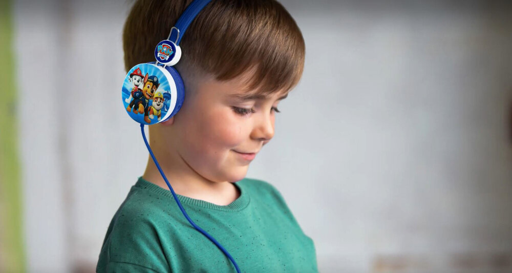 Dziecko nosi niebieskie słuchawki z motywem postaci z bajki. Słuchawki mają kolorowy nadruk z postaciami zwierząt.