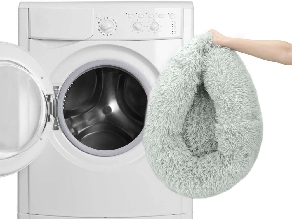 Antypoślizgowy i odporny na wilgoć spód legowiska uniwersalnego MUFART 15294. Ręka trzyma szare, puszyste legowisko dla psa i wkłada je do otwartego bębna pralki, co symbolizuje możliwość prania produktu. Tło jest białe.