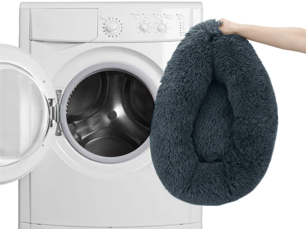 Antypoślizgowy i odporny na wilgoć spód legowiska uniwersalnego MUFART 15298. Ręka trzyma szare, puszyste legowisko dla psa i wkłada je do otwartego bębna pralki, co symbolizuje możliwość prania produktu. Tło jest białe.