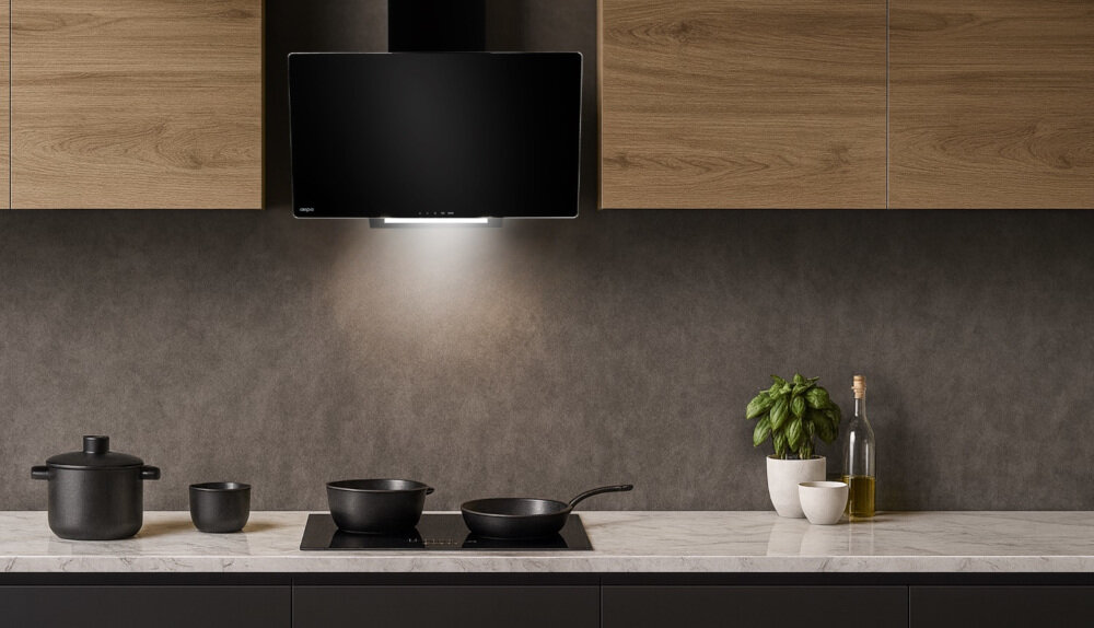 OKAP AKPO WK-4 Smart 60 Na zdjęciu widać kuchnię z czarną płytą grzejną na blacie z jasnego kamienia oraz czarnym okapem ściennym pod szafkami w kolorze drewna. Na blacie stoją czarne garnki i miski, doniczka z bazylią oraz butelka z oliwą, co podkreśla elegancki, minimalistyczny wystrój.