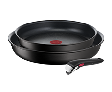 Na obrazie widoczne są dwie czarne patelnie z czerwonym okrągłym wzorem na środku oraz odłączany uchwyt z czerwonym przyciskiem. Patelnie mają gładką powierzchnię i są ułożone jedna na drugiej.