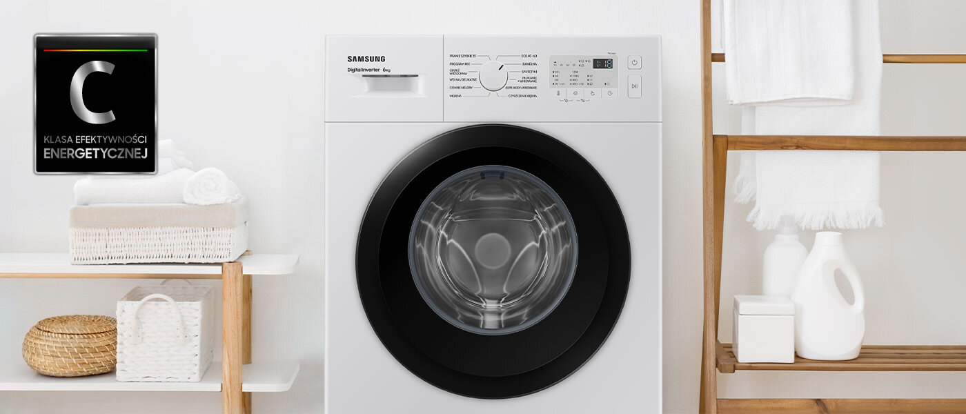 Pralka o białej obudowie z czarnym panelem wokół drzwi, z widocznym logo Samsung i panelem sterowania. Obok pralki znajduje się półka z ręcznikami i koszykiem, a w rogu widoczna jest ikona z napisem \'Klasa efektywności energetycznej C\'.