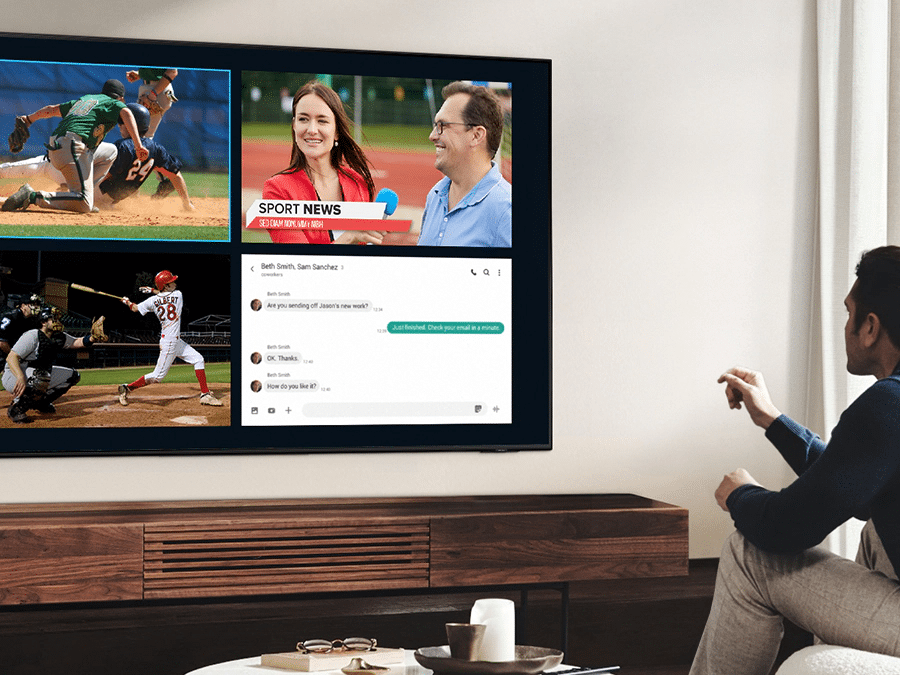 Чоловік використовує QLED Multi View, щоб одночасно дивитися футбольний матч і читати новини на одному екрані.