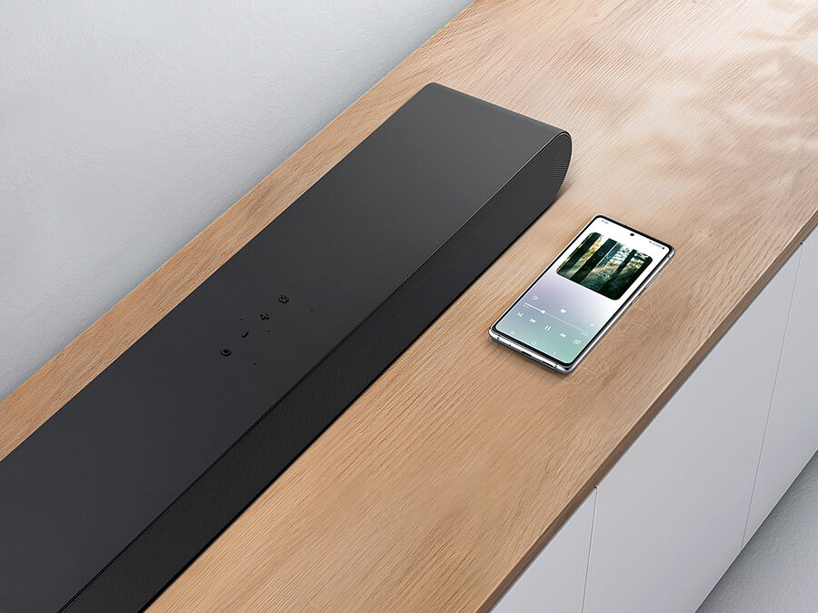 Czarny Soundbar Samsung S-seria HW-S60B i smartfon leżące na szafce. HW-S60B/EN