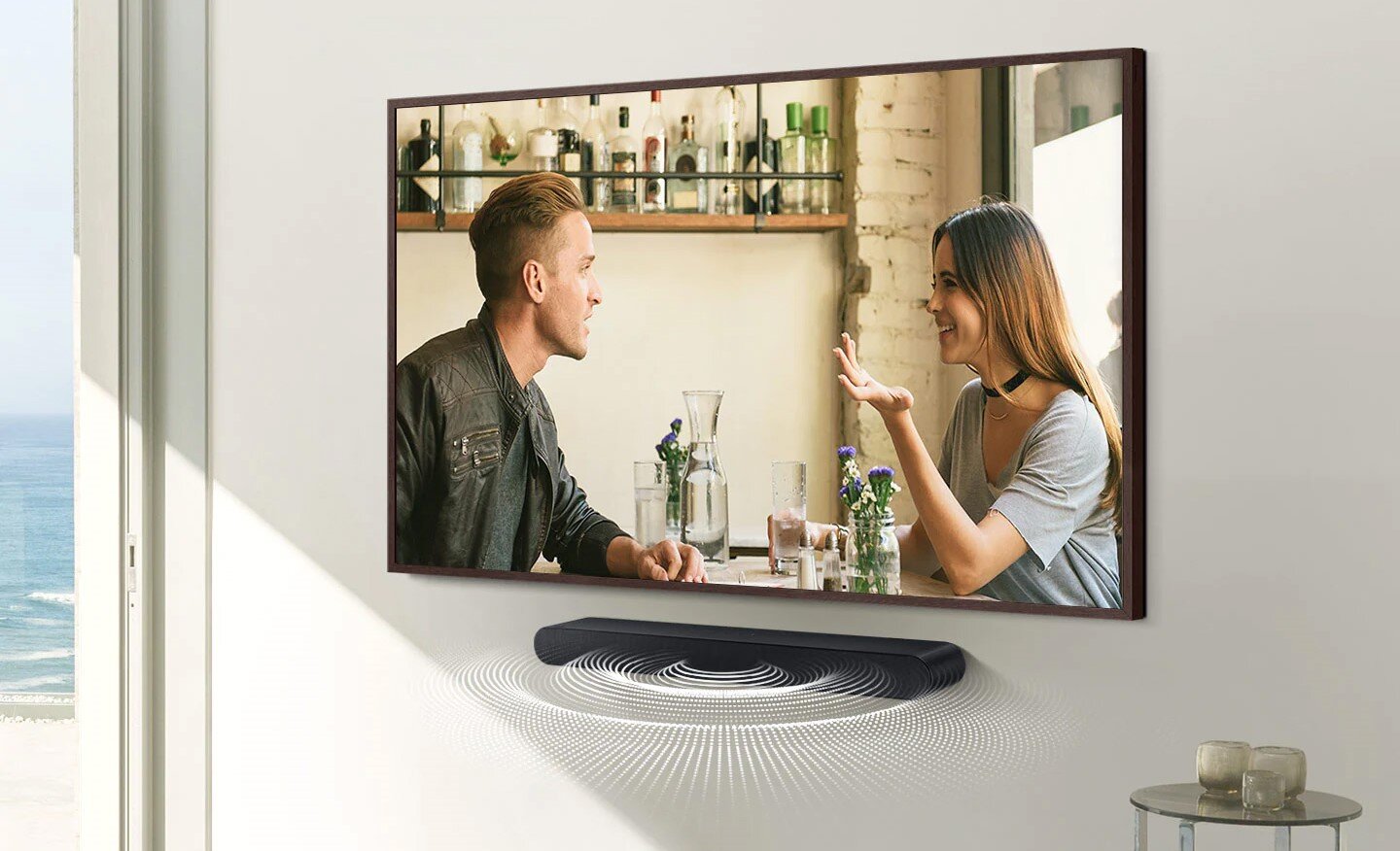 Dzwięki rozchodzące się z czarnego soundbara wiszącego na ścianie pod telewizorem. HW-S60B/EN