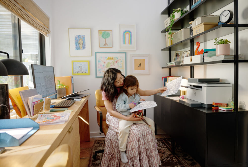 Urządzenie wielofunkcyjne HP LaserJet Enterprise MFP M430f Automatyczny druk dwustronny urządzenie postawione na szafce w domowym biurze kobieta siedząca na krześle z dzieckiem na kolanach i trzymająca wydruki