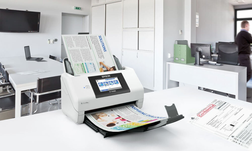 Skaner EPSON WorkForce DS-790WN Wi-Fi prezentacja skanera od przodu pod kątem na biurku wchodząca i wychodząca kartka w tle jasne biuro