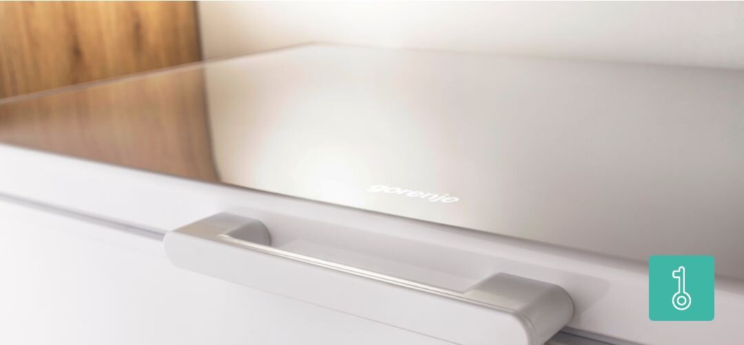 ZAMRAŻARKA GORENJE FH25EAW Fragment zewnętrznej pokrywy i uchwytu zamrażarki skrzyniowej Gorenje widzianej z boku, z ikoną symbolizującą wygodne otwieranie zamek, zabezpieczenie przed dziećmi, ochrona żywności