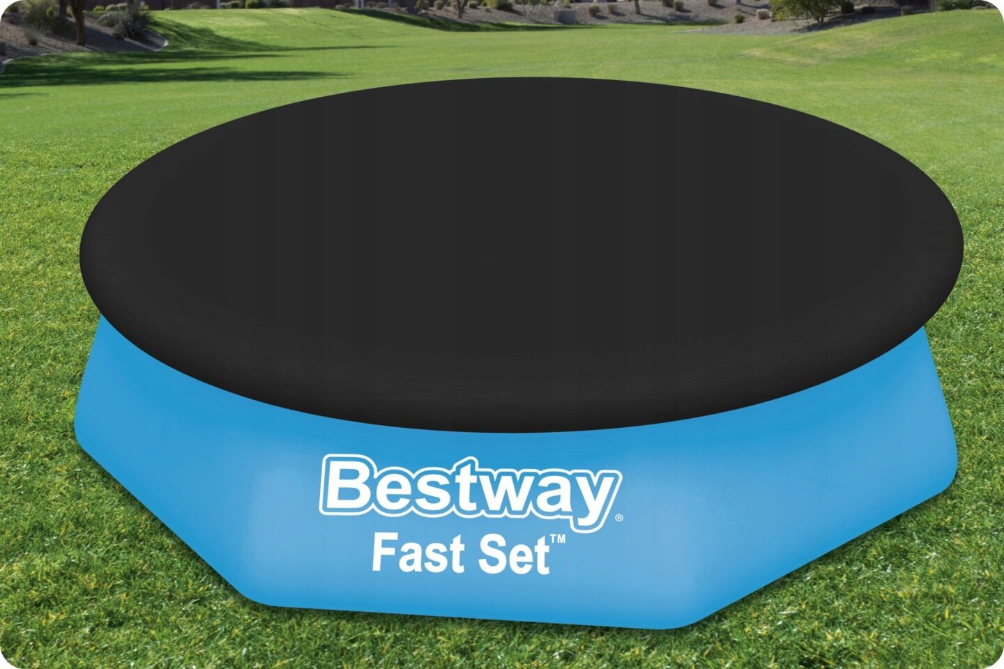 Na trawie znajduje się niebieski basen z czarną pokrywą, na którym widnieje napis \'Bestway Fast Set\'.