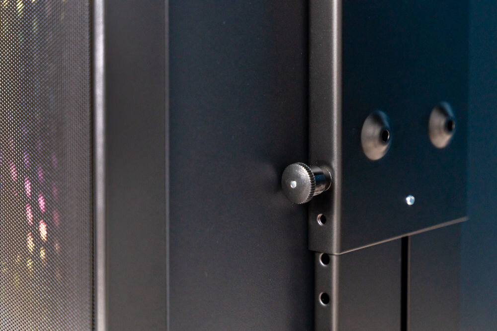 Uchwyt biurkowy do obudowy PC ART M-01 Zbliżenie na pokrętło blokujące uchwytu biurkowego, które zabezpiecza komputer przed przesunięciem. Widoczne są otwory wentylacyjne i metalowa konstrukcja obudowy komputera.