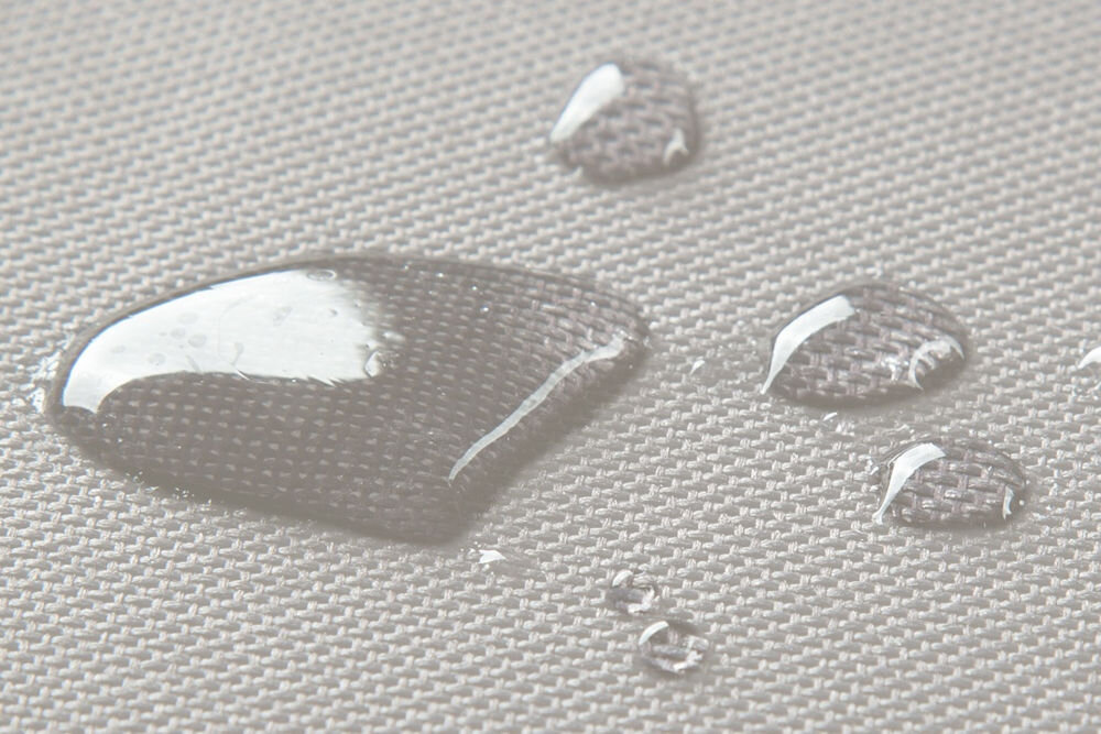 Legowisko dla psa BEDDOG Zara XXL bezowyZbliżenie ukazujące właściwości materiału: krople wody spoczywają na szarej, tkaninowej powierzchni legowiska, demonstrując wodoodporność materiału.