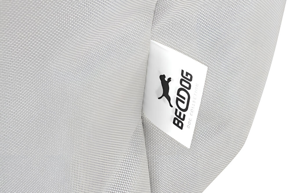 Legowisko dla psa BEDDOG Zara XXL bezowy Bardzo bliskie ujęcie na wszytą w materiał metkę z logo BEDDOG DOG COLLECTION (z sylwetką psa nad tekstem). Materiał legowiska jest jasnobezowy i teksturowany.