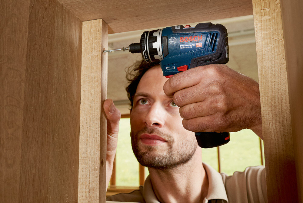 Wiertarko-wkrętarka BOSCH Professional GSR 12V-35 FC 06019H3000 pomieszczenie drewniana półka osoba przykręca śrubkę do ścianki widoczne oświetlenie na ściance wbudowane oświetlenie LED doświetla miejsce pracy pozwala szybciej i dokładniej ustawić nasadkę na śrubie zmniejszając ryzyko poślizgu i uszkodzenia elementów