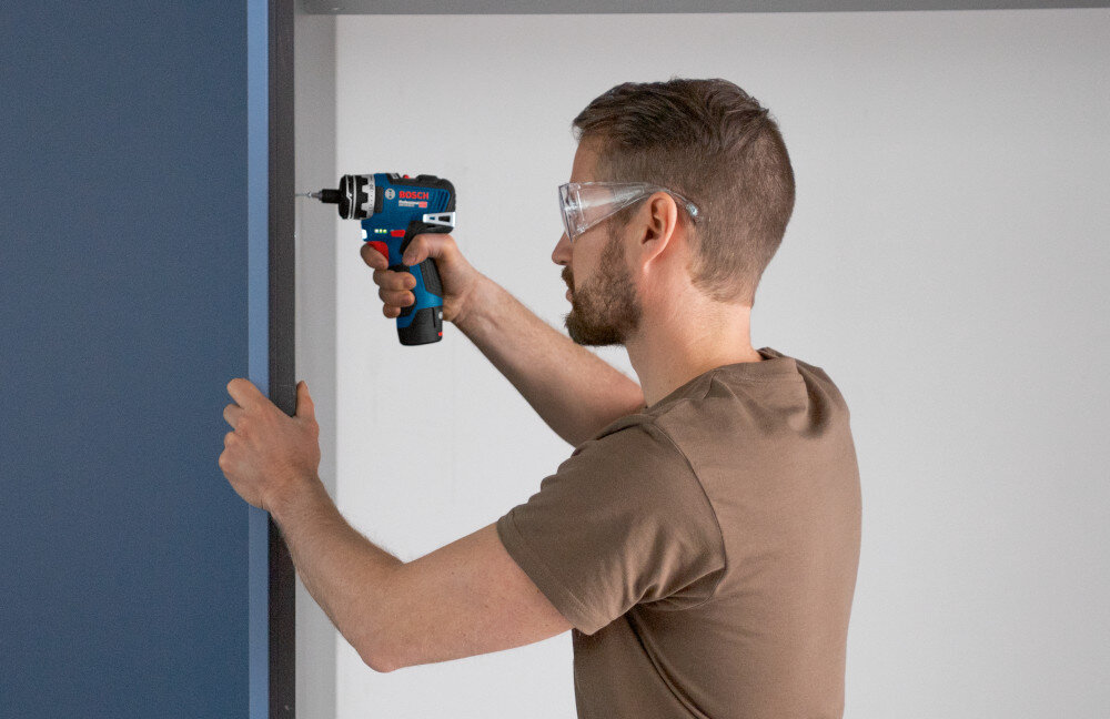 Wiertarko-wkrętarka BOSCH Professional GSR 12V-35 FC 06019H3000 pomieszczenie osoba przykręca śrubkę do drewnianej ściany silnik bezszczotkowy ogranicza straty energii i nagrzewanie dłuższy czas pracy na jednym akumulatorze rzadsze przerwy serwisowe i stabilna moc system EMP chroni napęd przed przeciążeniem