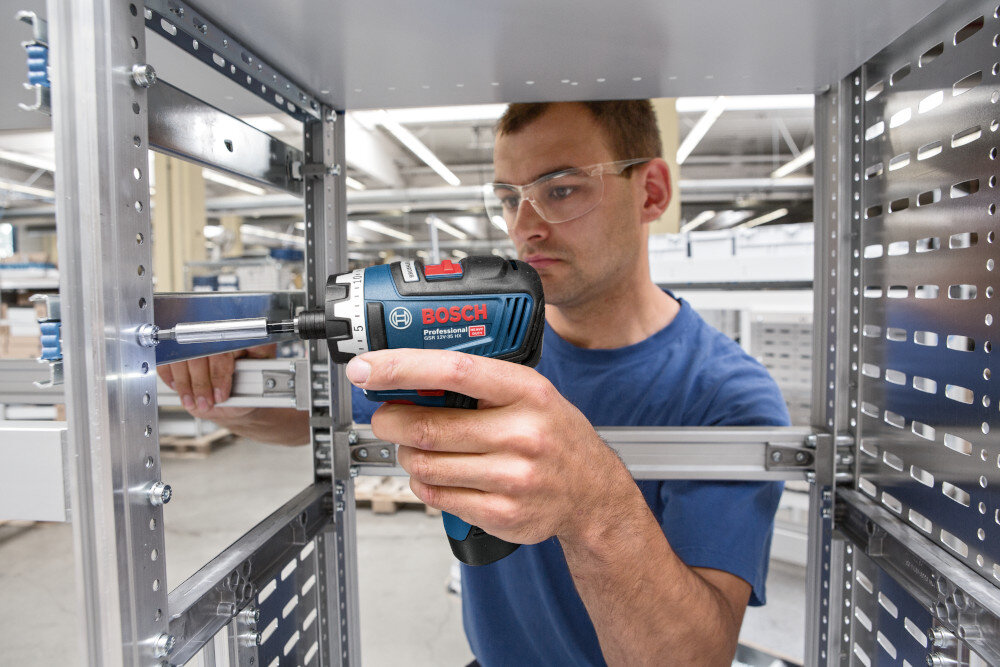 Wiertarko-wkrętarka BOSCH Professional GSR 12V-35 FC 06019H3000 pomieszczenie hala metalowa konstrukcja osoba przykręca śrubę do metalowej konstrukcji specjalny system ochronny elektroniczna ochrona ogniw ECP zabezpiecza akumulator przed przegrzaniem i przeciążeniem baterie zachowują pełną wydajność przez dłuższy czas