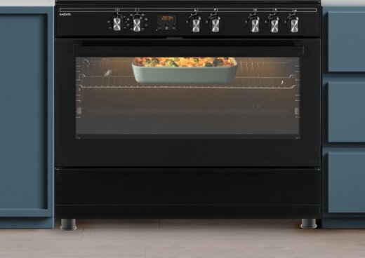 Zbliżenie na piekarnik z zapalonym światłem. W jego wnętrzu naczynie z jedzeniem.