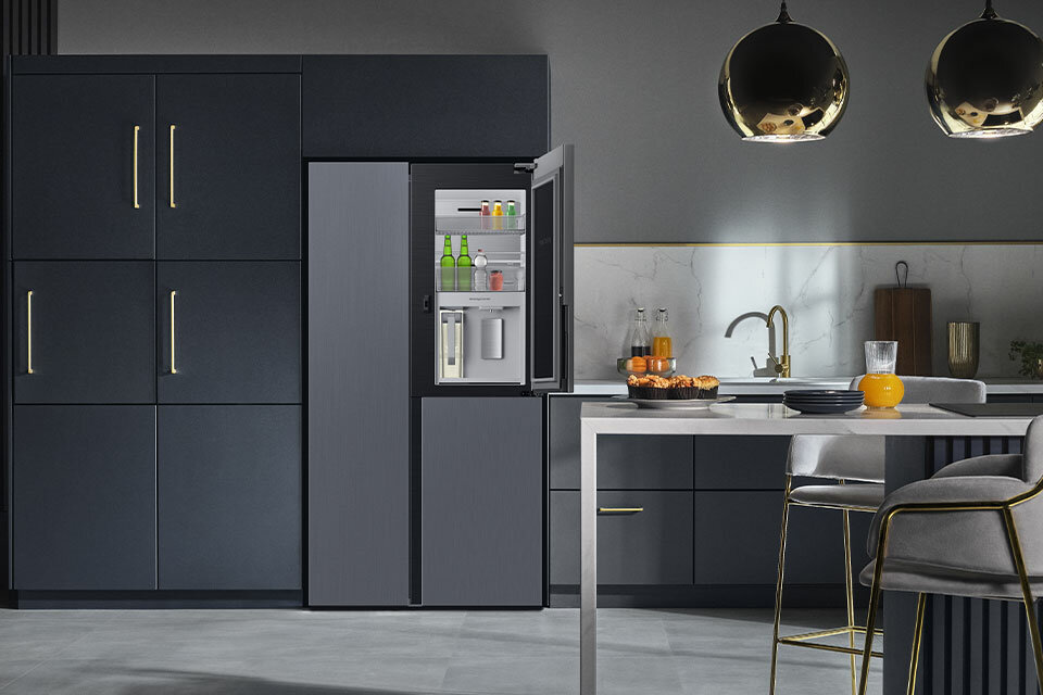 Zdjęcie pokazujące lodówkę Samsung z centrum napojów stojącą w przestronnej i nowocześnie urządzonej kuchni