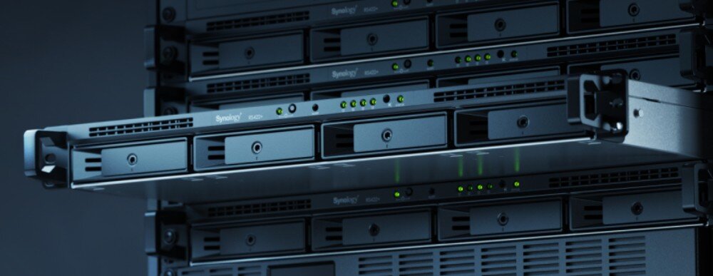 Serwer plików SYNOLOGY RS422+ Serwer sieciowy w obudowie rack wysunięty częściowo z szafy serwerowej, widoczne cztery kieszenie na dyski oraz diody kontrolne na panelu przednim, opis