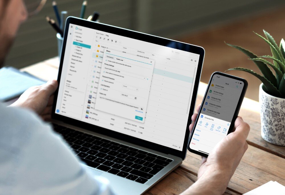 Serwer plików SYNOLOGY RS422+ Osoba pracująca przy biurku, korzystająca z laptopa z otwartym programem 'Drive' oraz trzymająca smartfon z tą samą aplikacją mobilną, działanie, zastosowanie