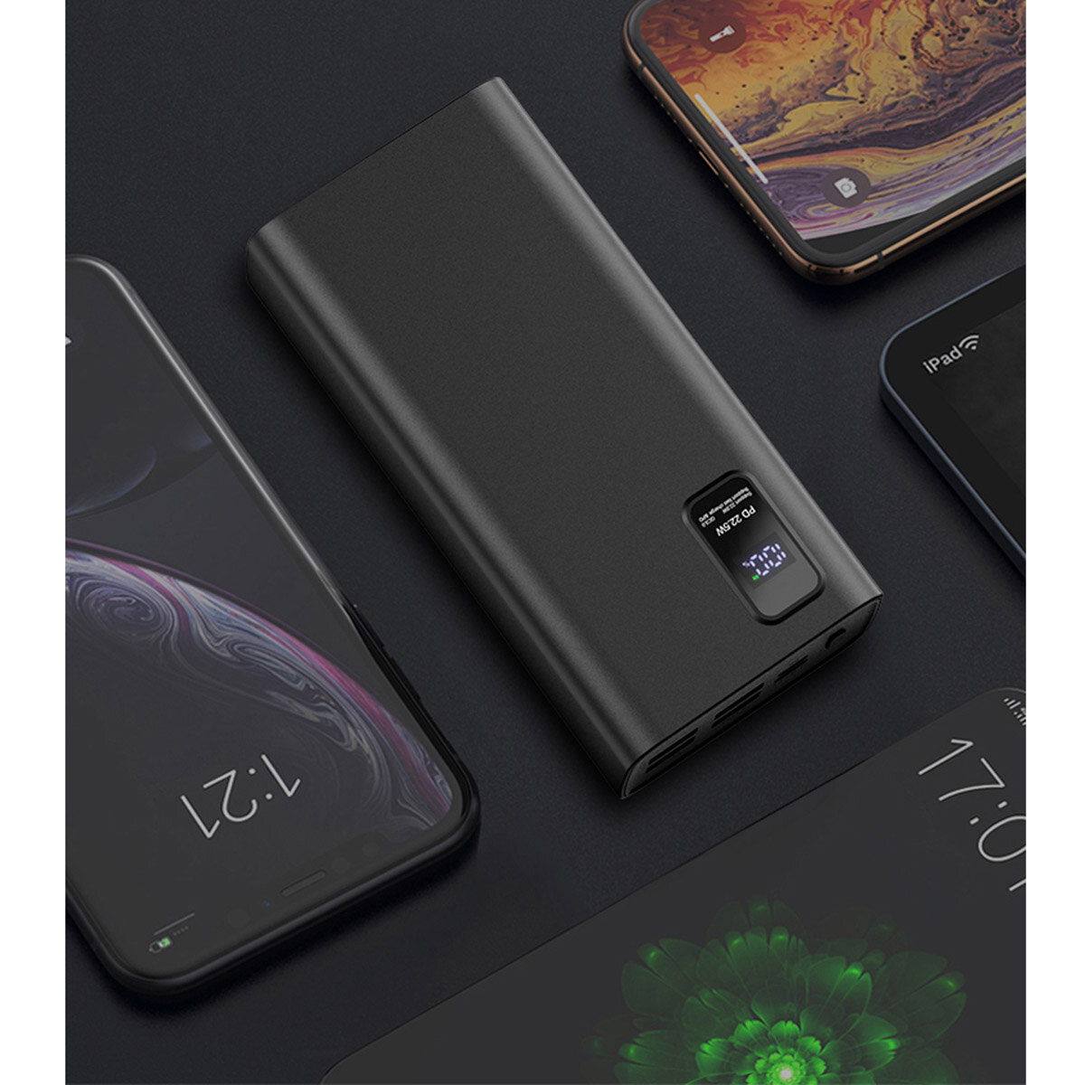 Czarny powerbank z wyświetlaczem LED pokazującym poziom naładowania, otoczony kilkoma smartfonami. Na wyświetlaczu widoczny jest tekst \'PD 3.0 QC 3.0\'.
