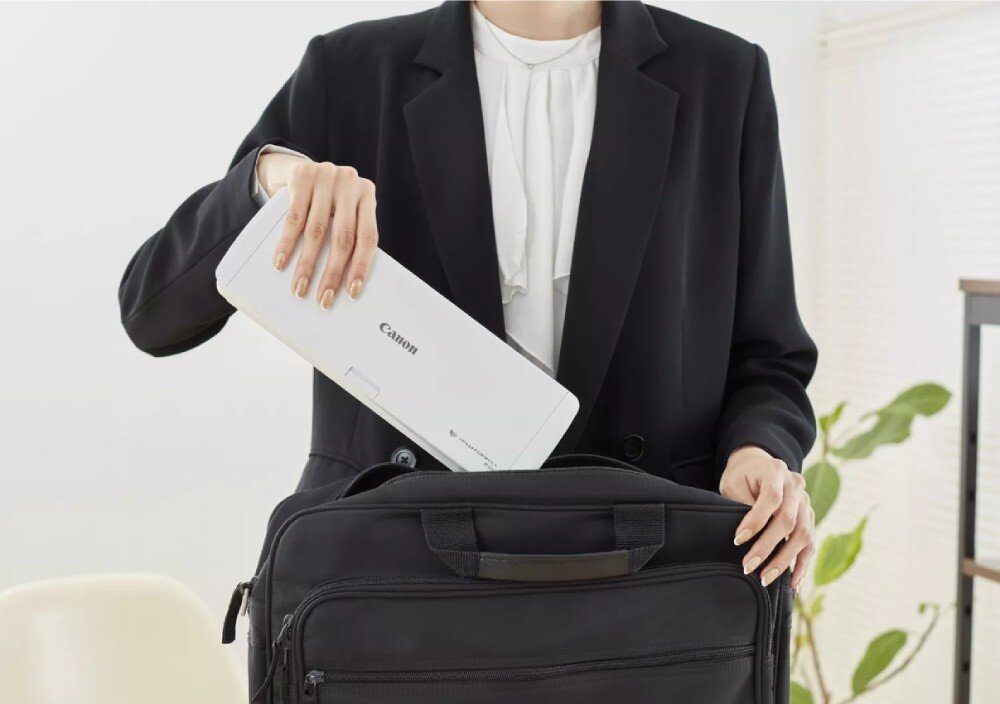 Skaner CANON imageFORMULA R10 Kobieta w czarnej marynarce wkłada białe podłużne urządzenie do czarnej torby na laptopa, wielkość, waga, mobilność
