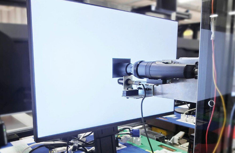Monitor EIZO ColorEdge CG2700S Zdjęcie pokazujące proces kalibracji monitora w warunkach laboratoryjnych. Ekran świeci jasnym światłem, a do jego powierzchni przyłożone jest urządzenie pomiarowe, kalibracja, dokładność, osłona ekranu