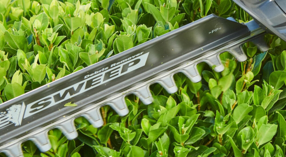 Nożyce do żywopłotu RYOBI RY18HT50A-0 500mm 18V akumulatorowe ogród zbliżenie na ostrza w tle żywopłot dom drzewa szlifowane diamentowo faliste ostrza ogranicza strzępienie gałęzi wysoka prędkość pracy 1350 obr./min