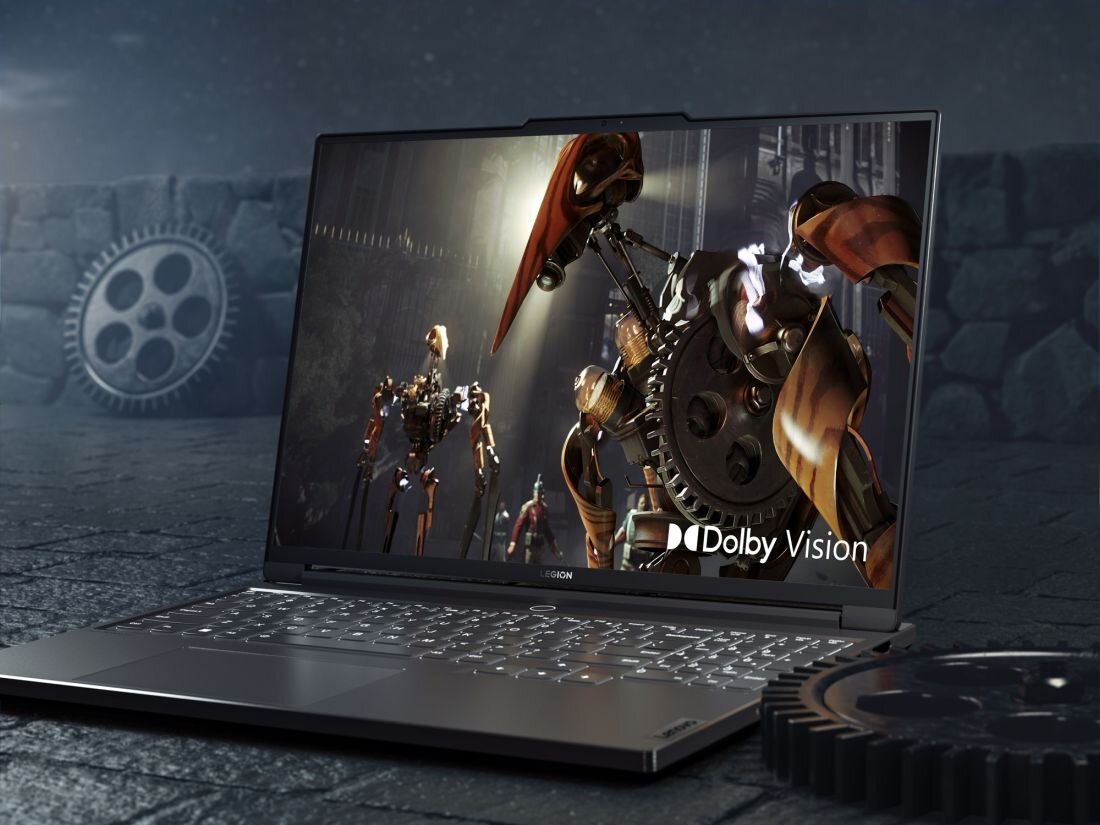 Laptop z wyświetlaczem pokazującym grafikę z robotami i napisem \'Dolby Vision\'. W tle widoczne są elementy mechaniczne, takie jak koła zębate.
