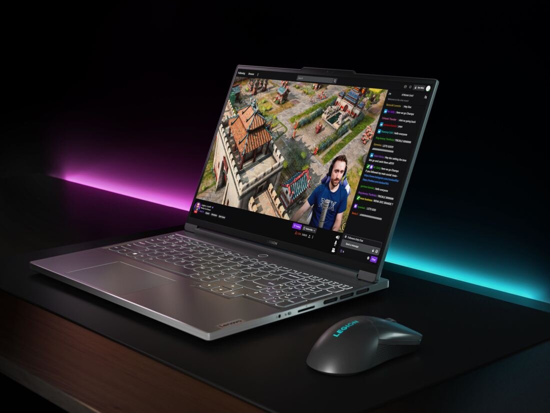Laptop z otwartym ekranem wyświetlającym grę komputerową i transmisję na żywo. Obok laptopa znajduje się myszka z logo \'Legion\'.