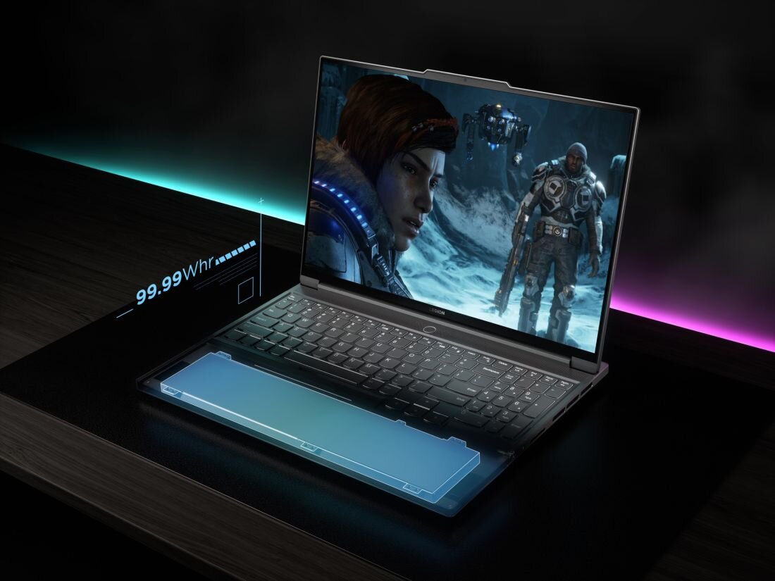 Laptop z otwartym ekranem, na którym wyświetlana jest scena z gry komputerowej. Obok laptopa widoczny jest napis \'99.99 Whr\'.