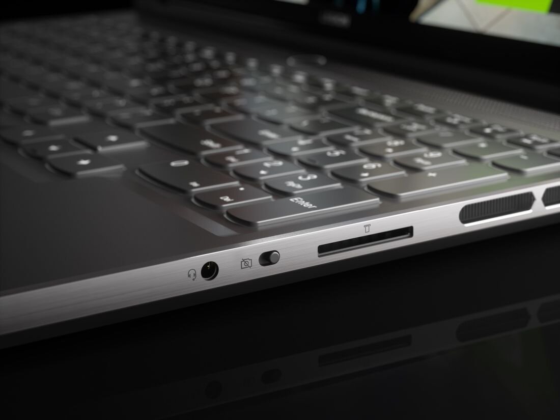 Zbliżenie na klawiaturę i boczny panel laptopa z widocznymi portami, w tym gniazdem audio, czytnikiem kart i przyciskiem. Obudowa jest metaliczna z wyraźnie zaznaczonymi klawiszami.