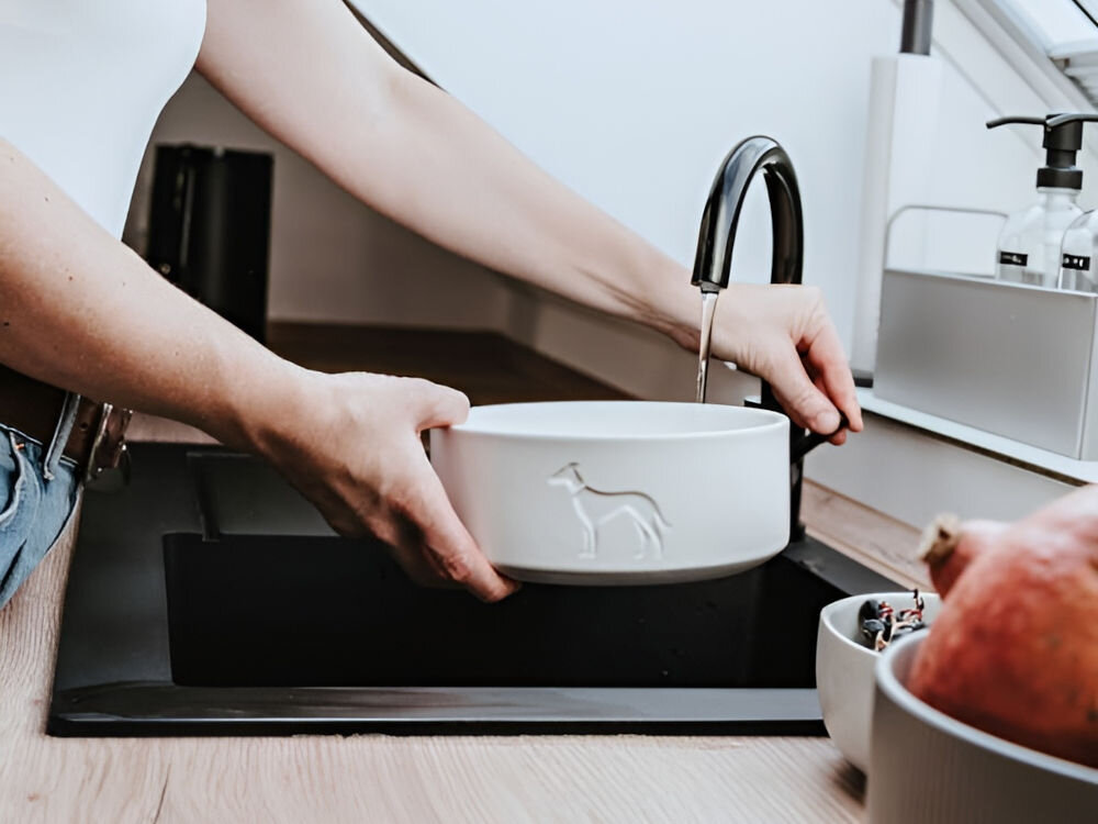 Miska ceramiczna dla psa HUNTER Osby 68982 Antracytowy, trwała i odporna na zarysowania, łatwa w czyszczeniu, możliwość mycia w zmywarce - Osoba napełnia wodą białą, ceramiczną miskę dla psa w czarnym zlewie kuchennym.