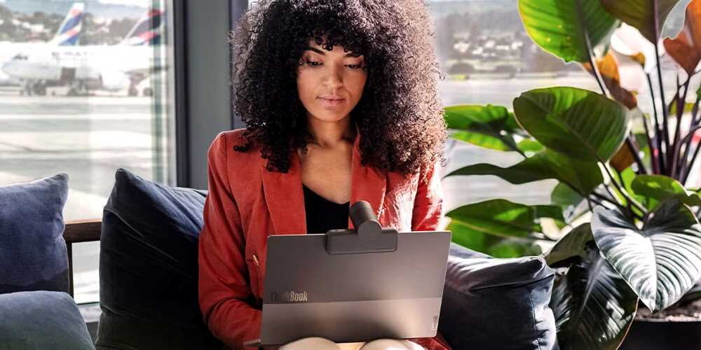 Laptop LENOVO ThinkBook 13x G2 - Kobieta o kręconych włosach siedzi na sofie, pracując na laptopie.