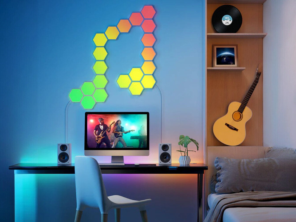 Lampa GOVEE H6061 Glide Hexa Wi-Fi, muzyka, rytm, dźwięk, impreza, Pokój muzyczny z monitorem Apple pokazującym koncert, głośnikami i siedmioma panelami Govee Hexa tworzącymi kształt nuty na ścianie, gitarą akustyczną i rośliną w tle.