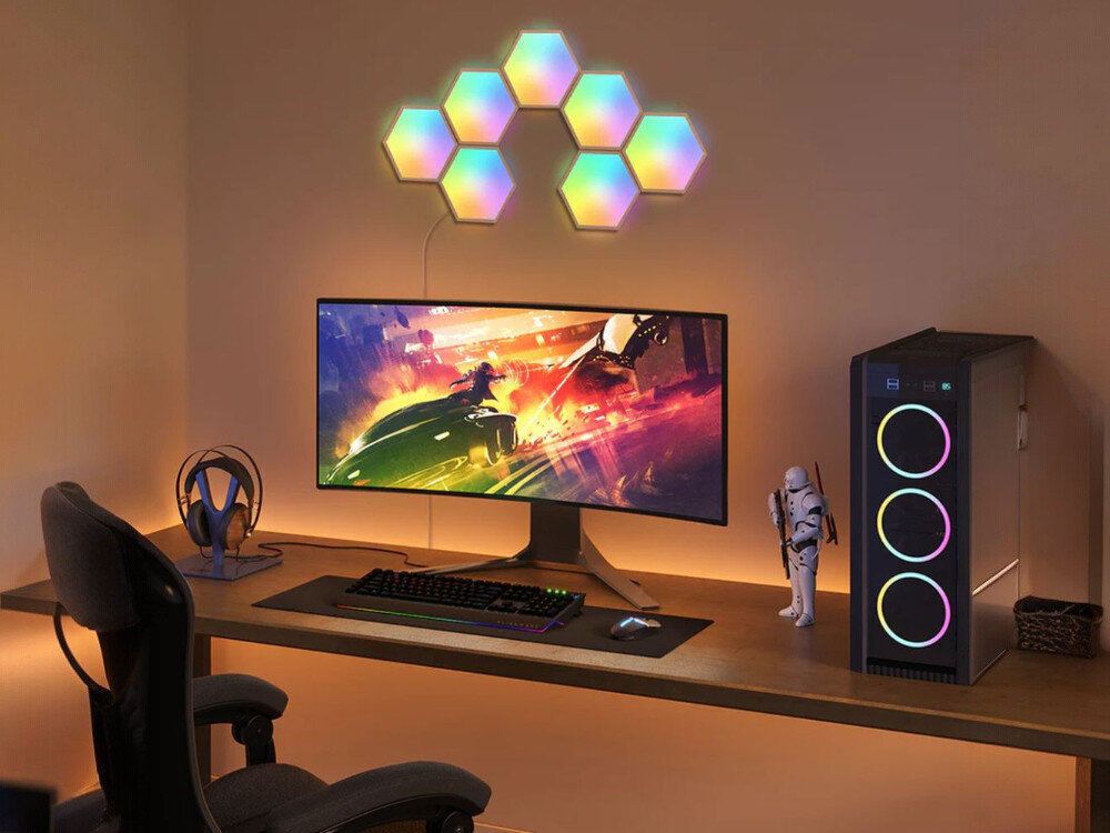 Lampa GOVEE H6061 Glide Hexa Wi-Fi, montaż, DIY, aplikacja, aranżacja, Gamingowy setup z zakrzywionym monitorem wyświetlającym futurystyczną grę, obok obudowy PC Razer z RGB, figurką Stormtroopera i siedmioma panelami Govee Lyra Hexa w gradientowych kolorach na ścianie.
