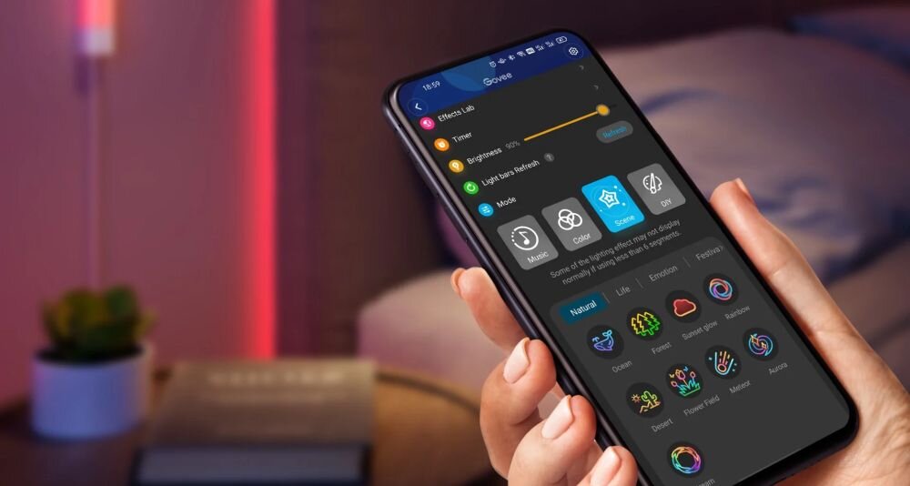 Lampa GOVEE H6062 Glide Wi-Fi/Bluetooth (7 szt.), sceny, nastrój, światło, emocje, Aplikacja Govee na smartfonie OnePlus w ciemnym trybie, z panelem sterowania oświetleniem: ikony scen, efektów pogodowych, kolorów i trybu snu, trzymana nad stolikiem nocnym.