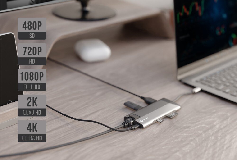 Hub NATEC Fowler Plus 8w1 Laptop podłączony do huba wieloportowego na drewnianym biurku z monitorem w tle.